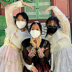 Three girls of Asian descent in traditional dress as well as face masks dance