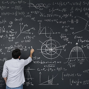 A physicist stands in front of a large blackboard working on equations