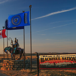 A sign and flags stand at an entryway to the land of the Blackfeet Nation