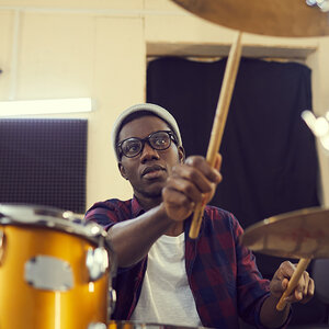 An African American drummer seated behind his drum kit strikes the cymbals with his drum sticks. An African American drummer seated behind his drum kit strikes the cymbals with his drum sticks.