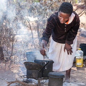 An African woman cooking food over a smoky open fire. An African woman cooking food over a smoky open fire.