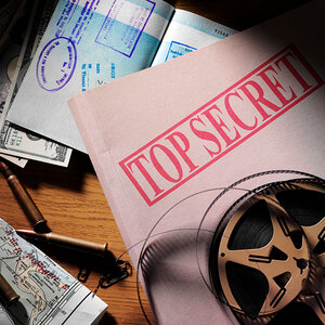 A desktop covered with top secret files, money and a spy’s passport. A desktop covered with top secret files, money and a spy’s passport.