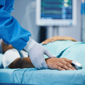 A person laying in a hospital bed holding a doctor's hand.