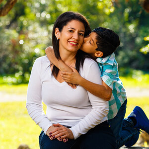 A Latinx boy hugs hus mother as they sit beneath a tree. A Latinx boy hugs hus mother as they sit beneath a tree.