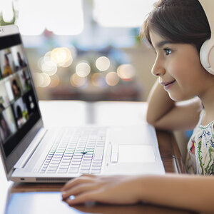 A girl wearing headphones looks at her classmates on a Zoom classroom on her computer A girl wearing headphones looks at her classmates on a Zoom classroom on her computer
