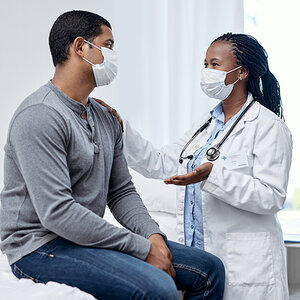 Doctor and patient of color wearing masks talking.