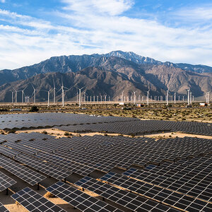 A solar farm with windmills and mountains in the background.