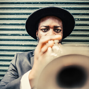 A jazz trumpter, the bell of the instrument near the camera, looks at the photographer.