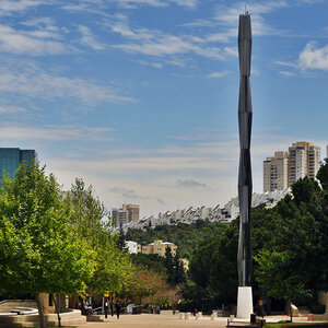 A verdant college campus with a tall tower-like sculpture in the foreground.