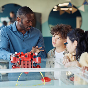 An African-American teacher demonstrates a robotic device to his young students.