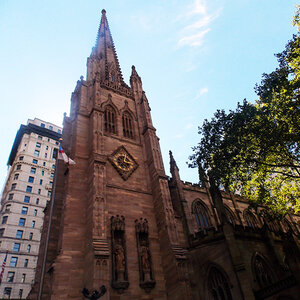 The clock tower of an old church surrounded by office buildings and trees.