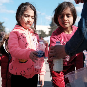A relief worker is pouring milk into bottles for two young girls. A relief worker is pouring milk into bottles for two young girls.