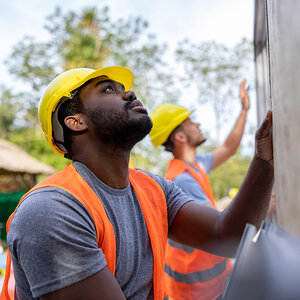 Construction workers wearing yellow hardhats and orange safety vests raising the wall of a house. Construction workers wearing yellow hardhats and orange safety vests raising the wall of a house.