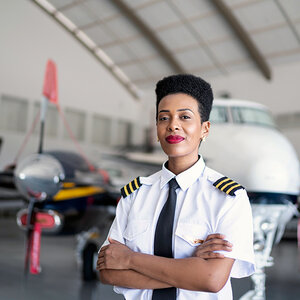 An African American woman pilot stands in front of an airplane. An African American woman pilot stands in front of an airplane.