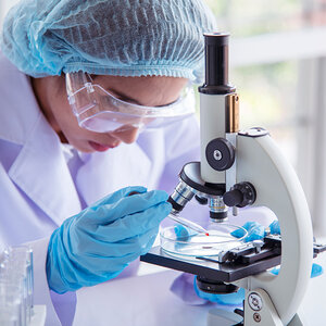 A woman scientist in a laboratory wearing protective clothing using a microscope.
