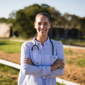 A young female doctor, wearing a stethoscope and a white coat, stands in a rural setting. A young female doctor, wearing a stethoscope and a white coat, stands in a rural setting.