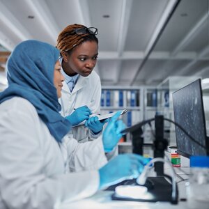 Two women scientists of color in a lab looking at a computer screen.