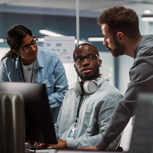 Two men and a woman are having a discussion in a computer lab.