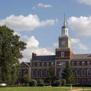 An elegant red brick college building with a clock tower and cupola surrounded by trees - Howard University.