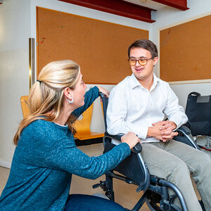 A man with down syndrome sits in a wheelchair with a woman sitting beside him. A man with down syndrome sits in a wheelchair with a woman sitting beside him.
