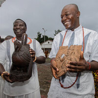 Two African men hold antiquities known as the Benin Bronzes. Two African men hold antiquities known as the Benin Bronzes.