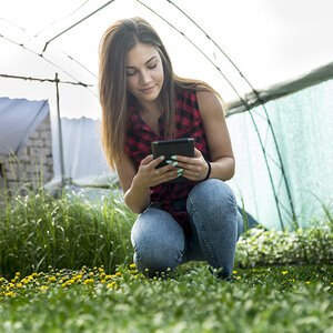 A young woman check on her plants in a greenhouse.
