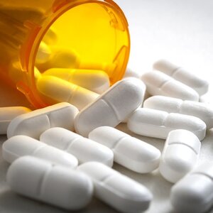 White Hydrododone pills spilling out of an amber prescription medication bottle.