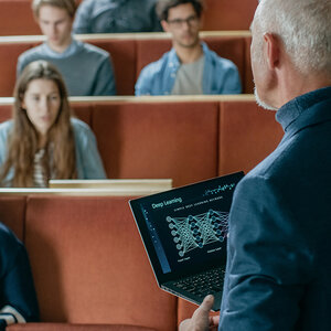 A professor lectures to his class using a laptop with a graphic that reads Deep Learning. A professor lectures to his class using a laptop with a graphic that reads Deep Learning.