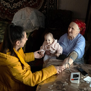 A healthcare worker checks the blood pressure of an old woman who is holding her grandchild.