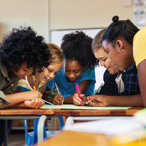 A group of elementary school children and their teacher huddle during a lesson. A group of elementary school children and their teacher huddle during a lesson.