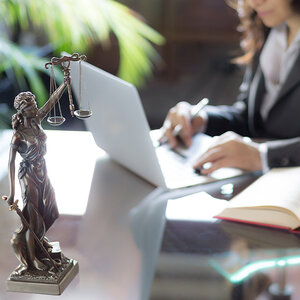 A woman lawyer working on a computer with a figurine of Lady Justice in the foreground. A woman lawyer working on a computer with a figurine of Lady Justice in the foreground.