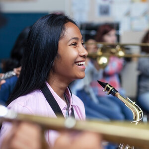 A smiling girl holds a saxophone while playing in a jazz band. A smiling girl holds a saxophone while playing in a jazz band.