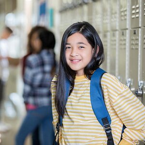 A young girl in middle school stand by her locker.