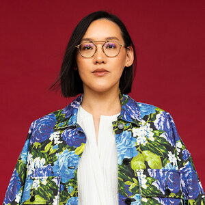 An Asian woman wearing glasses and a colorful jacket in front a red wall – a photo of Krstine Kuan. An Asian woman wearing glasses and a colorful jacket in front a red wall – a photo of Krstine Kuan.