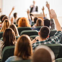 A college lecture hall with students raising their hands. A college lecture hall with students raising their hands.