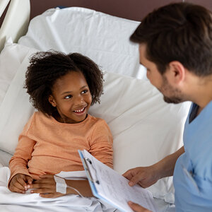 A girl in a hospital bed smiles as her male nurse checks in on his patient. A girl in a hospital bed smiles as her male nurse checks in on his patient.