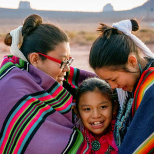 A smiling Native American girl surrounded by two older Native females.