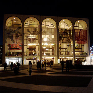 The façade of a modern opera house at night brilliantly lit from within – the Metropolitan Opera House.
