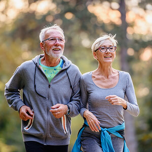a senior couple jogs together in a park.